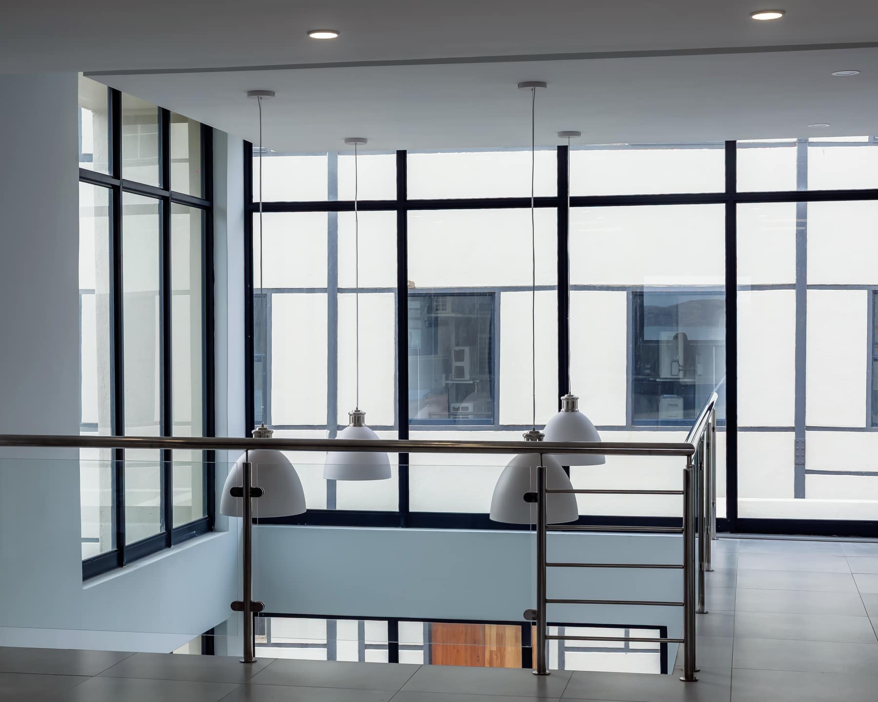 Stairwell and upper landing lit by suspended pendant fittings against full-height glazing